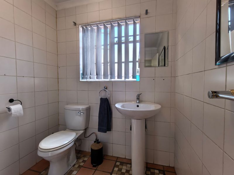 A functional bathroom featuring a pedestal basin, toilet, and fully tiled walls and floors, currently showing signs of wear and dated finishes.