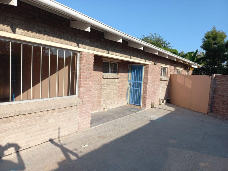 A view of the rear exterior of the house featuring face brick construction, paved ground area, and security bars on windows and doors.