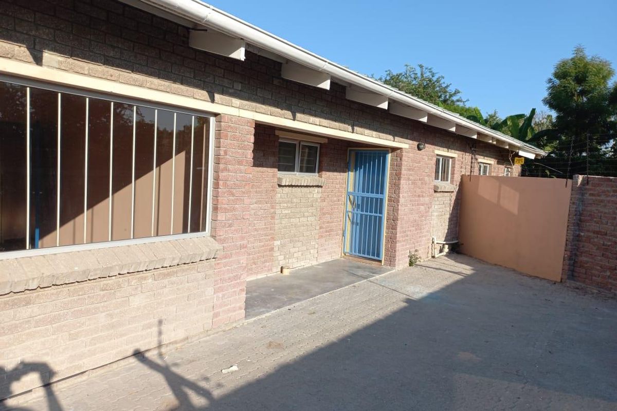 A view of the rear exterior of the house featuring face brick construction, paved ground area, and security bars on windows and doors.