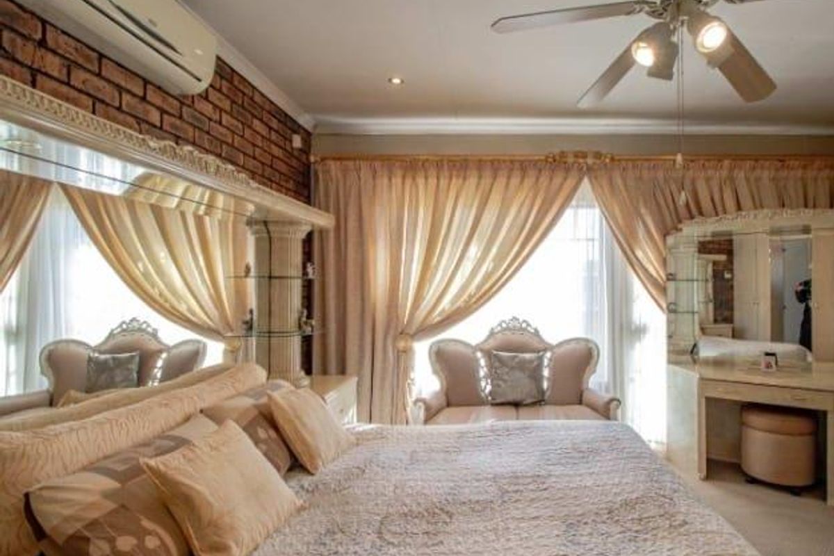 A bedroom featuring an exposed brick feature wall, split-system air conditioning, a ceiling fan, and a built-in vanity unit with integrated mirror.