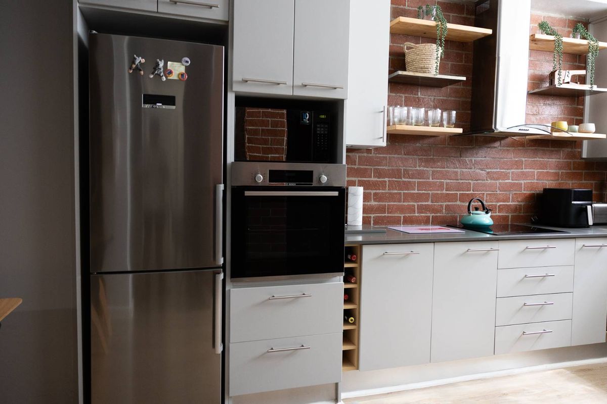 Modern kitchen featuring exposed brick walls, floating timber shelving, integrated cabinetry, and high-quality built-in appliances including an oven and microwave.