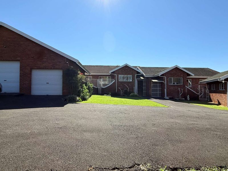 Front exterior view of a brick townhouse featuring multiple garage doors, a large asphalt driveway, and a well-maintained lawn area.