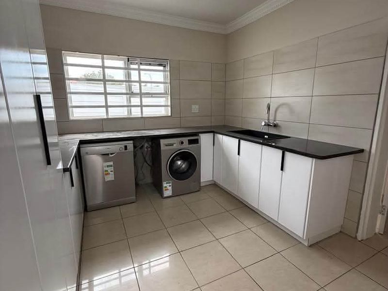 A clean and functional scullery featuring modern white cabinetry, dark stone countertops, tiled splashbacks, and integrated space for laundry appliances.