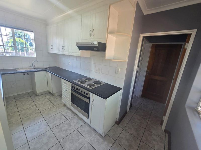 Functional kitchen featuring white cabinetry, dark laminate countertops, built-in oven with hob, and tiled flooring, offering a clean space ready for updates.