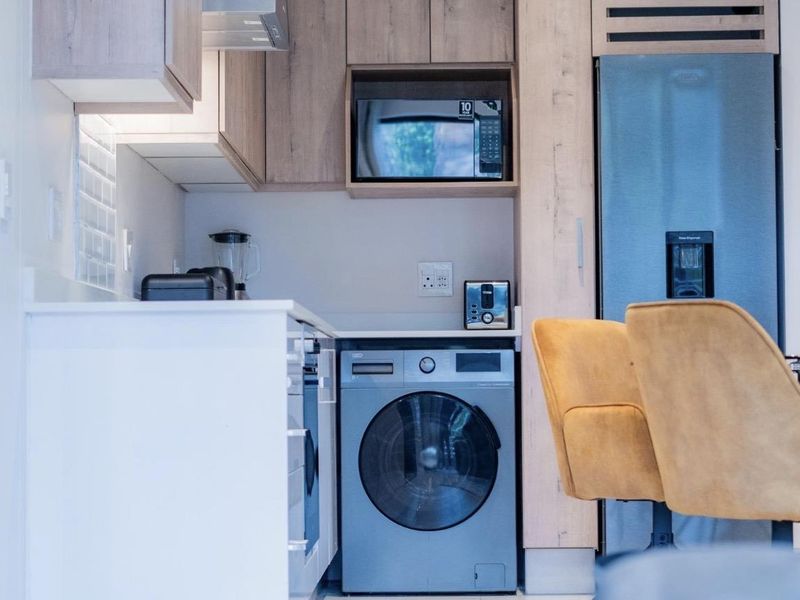Modern kitchen featuring light wood cabinetry, stone countertops, subway tile backsplash, and integrated appliances including a washing machine and fridge.