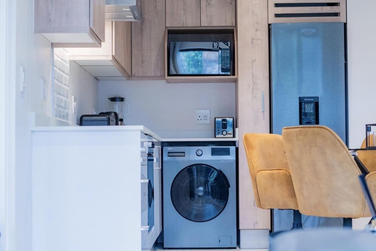 Modern kitchen featuring light wood cabinetry, stone countertops, subway tile backsplash, and integrated appliances including a washing machine and fridge.