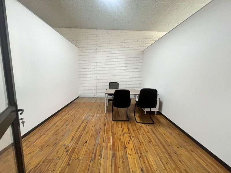 A functional office space featuring exposed white brickwork, timber flooring, and an acoustic tile ceiling, offering a clean and professional environment.