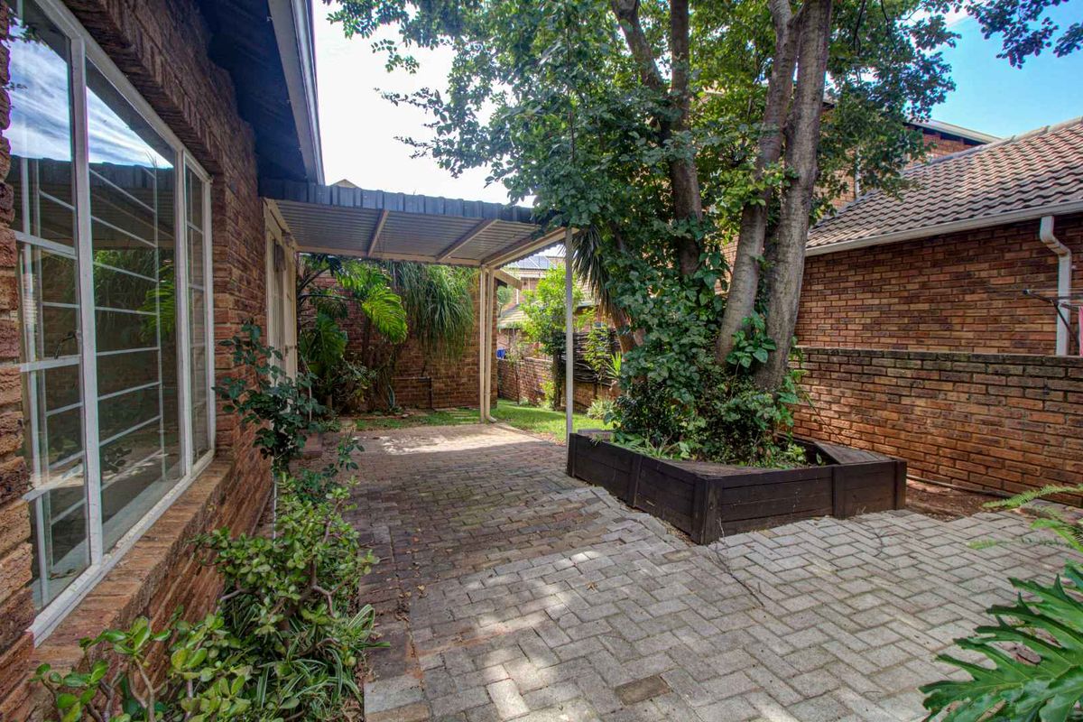 A private rear courtyard featuring paved flooring, a covered patio area, and a raised timber planter box set against a brick boundary wall.