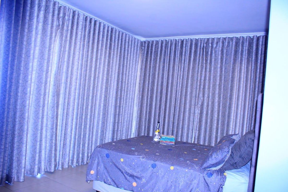A bedroom featuring full-length wall-to-wall curtains and tiled flooring.
