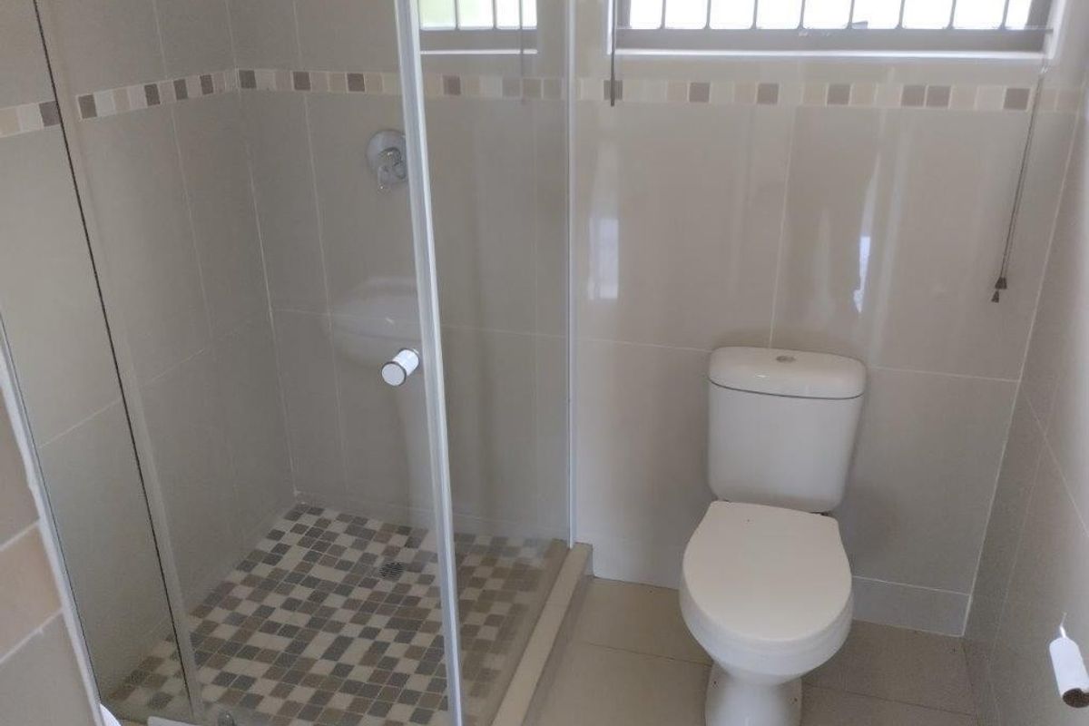 A clean, functional bathroom featuring a glass-enclosed shower, ceramic tiling, and a standard toilet.
