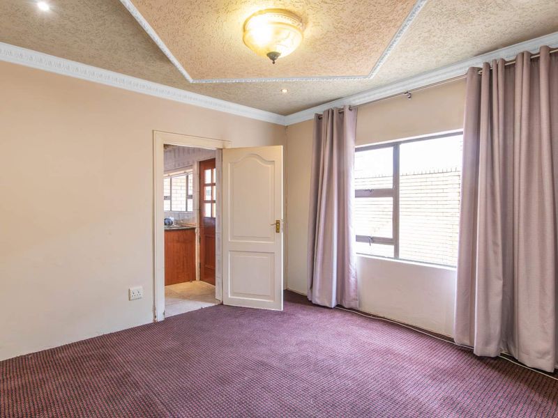 An empty bedroom featuring carpeted flooring, a textured ceiling with decorative coving, and a window with neutral curtains.