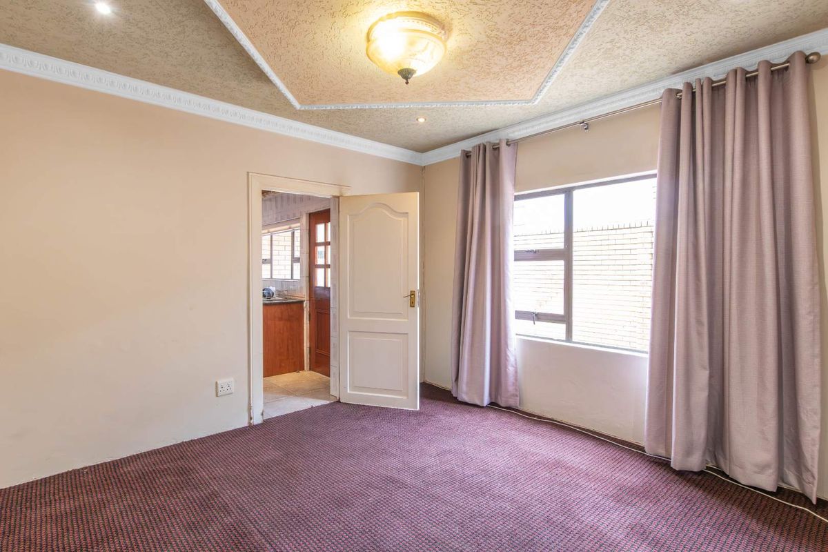 An empty bedroom featuring carpeted flooring, a textured ceiling with decorative coving, and a window with neutral curtains.
