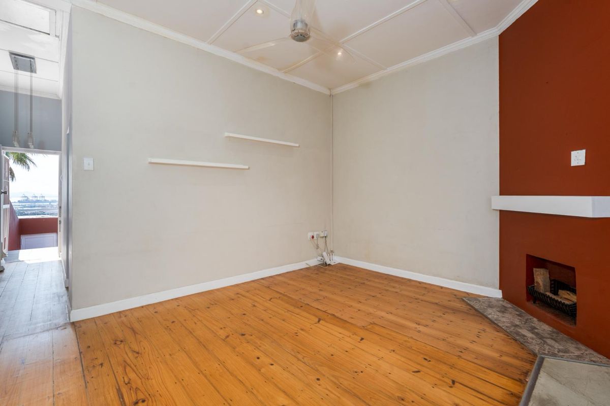 An empty living room featuring original timber flooring, a fireplace with a mantelpiece, and a ceiling fan, with access to an outdoor balcony area.
