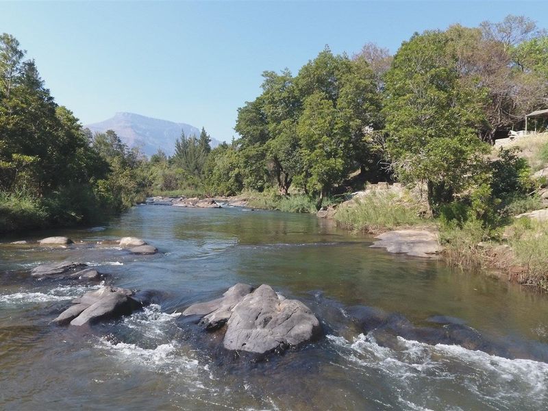 A scenic view of a flowing river with rocky outcrops, surrounded by lush trees and distant mountains on the farm property.