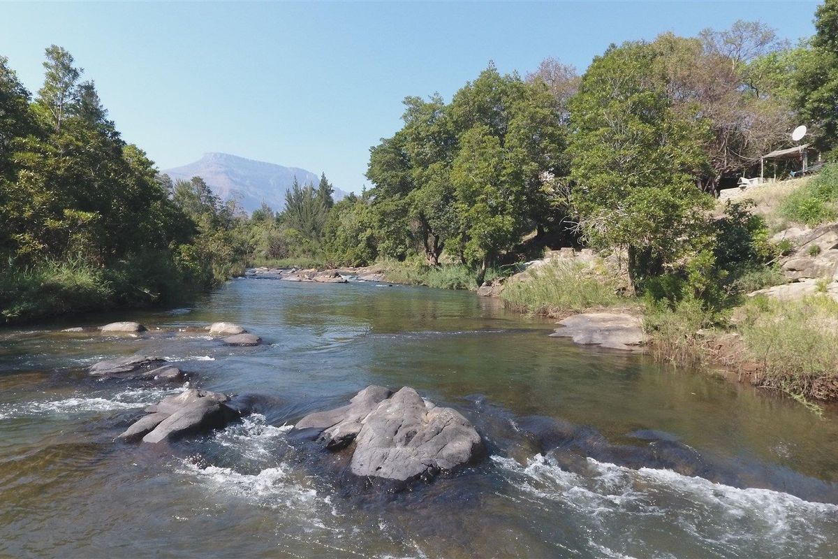 A scenic view of a flowing river with rocky outcrops, surrounded by lush trees and distant mountains on the farm property.