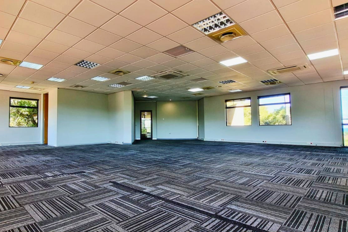 A spacious, open-plan office area featuring a suspended ceiling with recessed lighting, air conditioning, and durable carpet tiles, offering a versatile workspace.