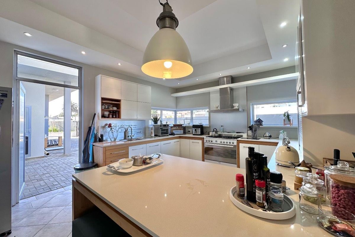 Modern kitchen featuring stone countertops, a central island, stainless steel gas stove with extractor fan, and direct access to an outdoor patio area.