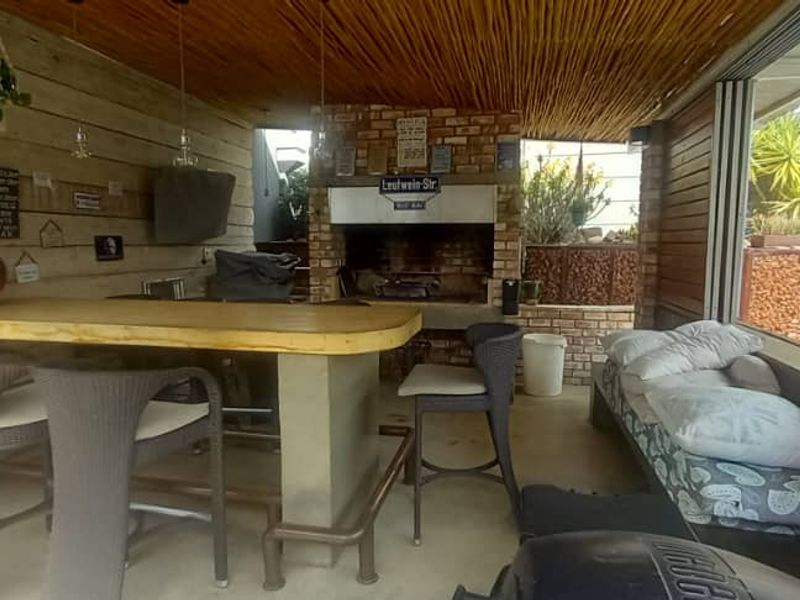 Covered outdoor entertainment area featuring a built-in brick braai, timber-clad walls, thatched ceiling, and a concrete bar counter overlooking the pool area.