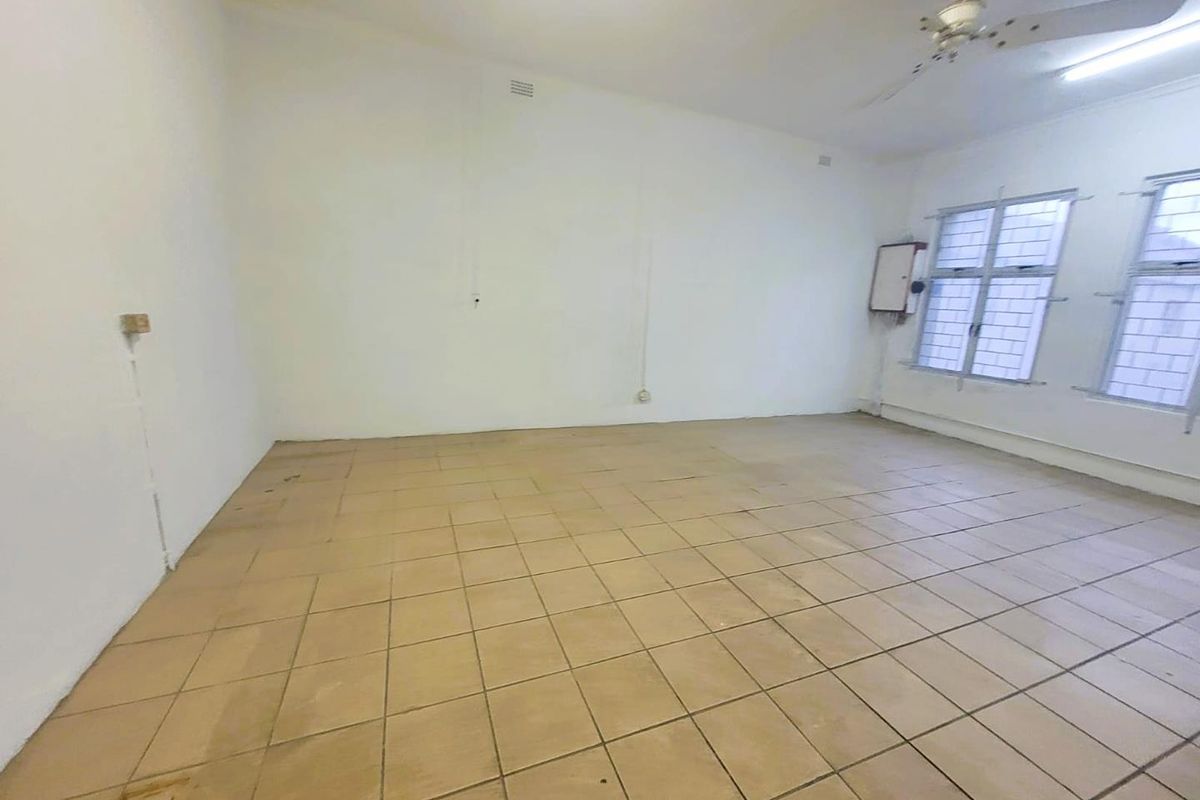 An empty, versatile room featuring tiled flooring, a ceiling fan, and security-barred windows, suitable for various commercial or residential uses.