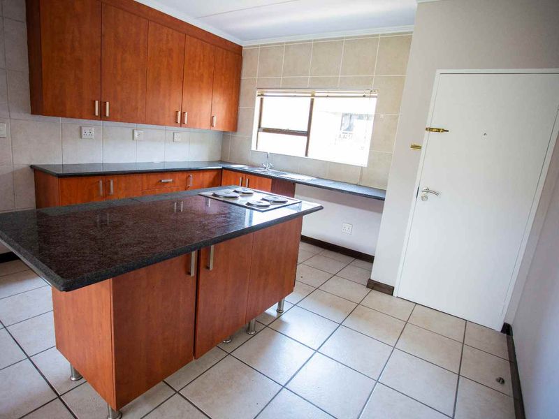 A functional kitchen featuring wooden cabinetry, granite countertops, a central island with a built-in hob, and tiled flooring throughout.