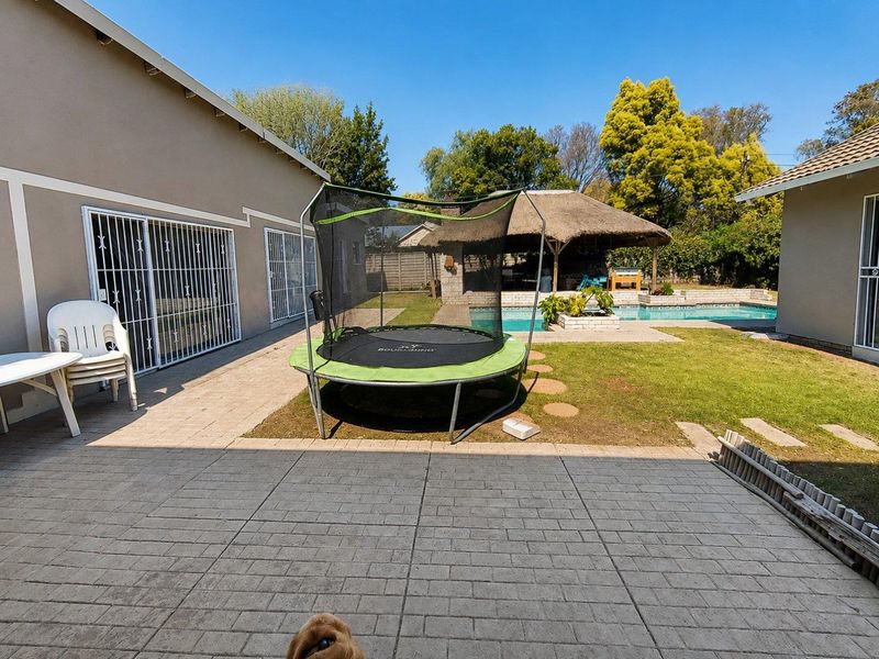 Rear garden area featuring a paved patio, swimming pool, and a thatched lapa, providing an outdoor entertainment space.