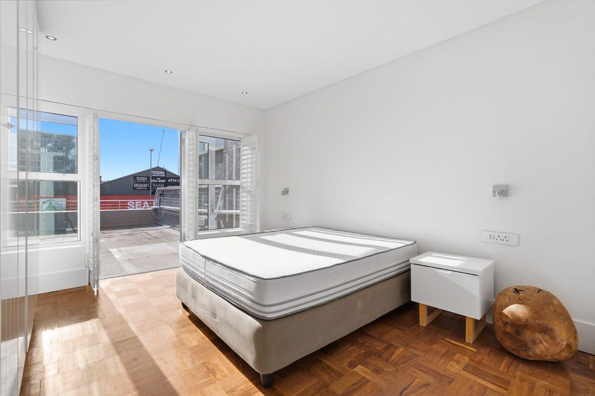 Bright bedroom featuring parquet flooring, recessed ceiling lighting, and large glass doors opening onto a private balcony.