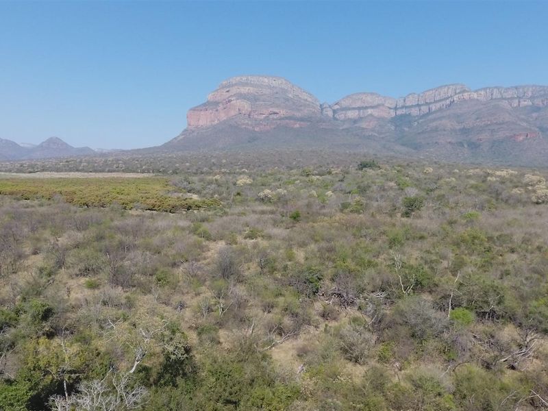 An expansive aerial view of the farm landscape featuring natural bushveld vegetation and prominent mountain ranges in the background.