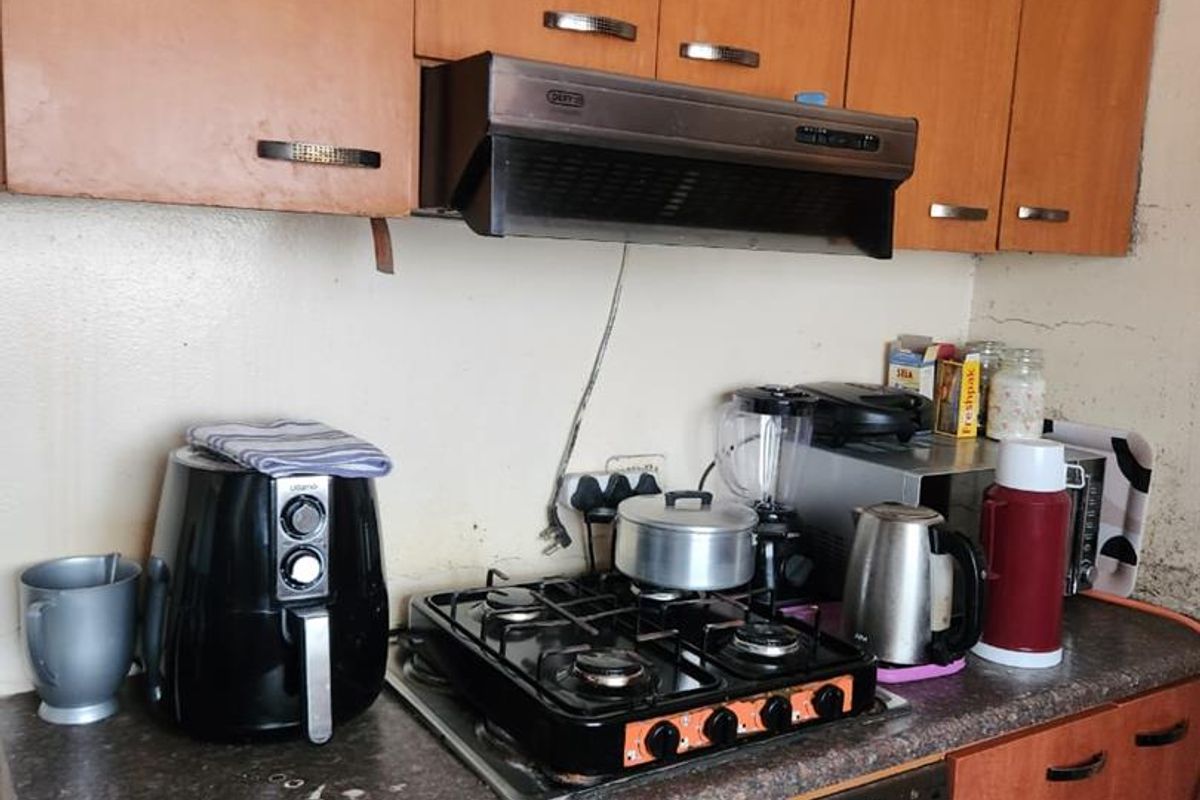 A functional kitchen featuring wooden cabinetry, a built-in oven, gas hob, and extractor fan, showing signs of wear and requiring cosmetic updates.