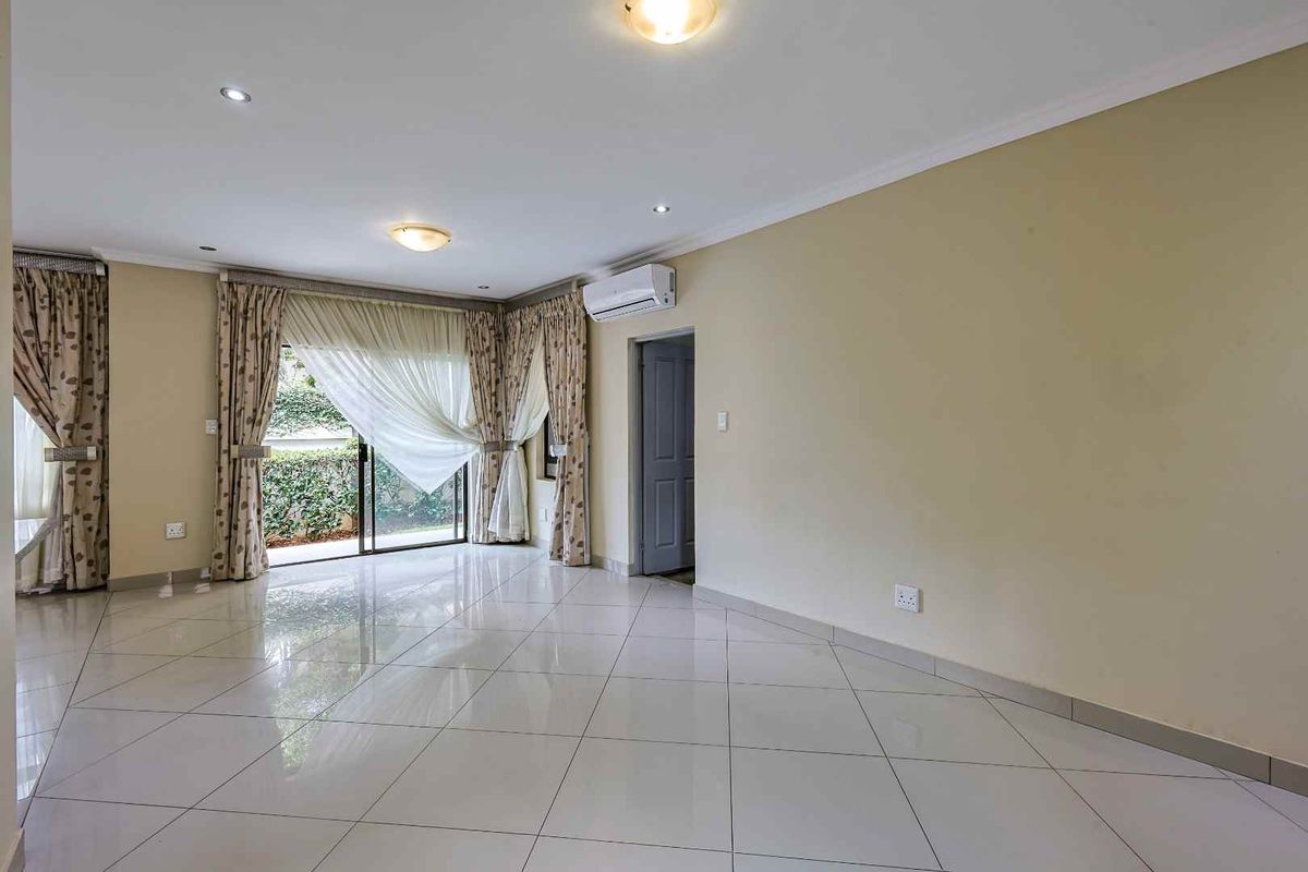 Spacious living area featuring polished floor tiles, a wall-mounted air conditioning unit, and sliding glass doors providing access to the exterior.
