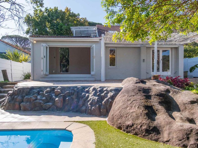 Rear exterior view featuring a swimming pool, tiled patio area with pergola, and unique natural rock landscaping elements.