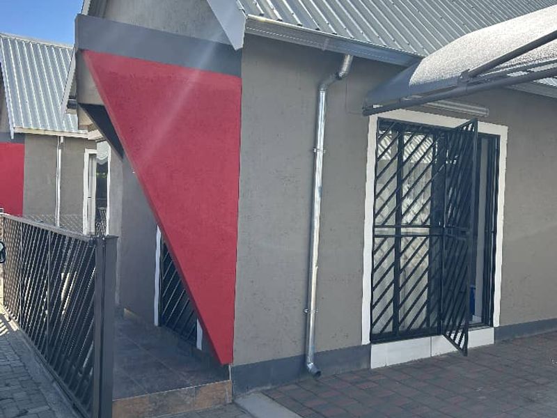 Front exterior view of an apartment unit featuring a metal roof, paved driveway, and secure entrance gate.