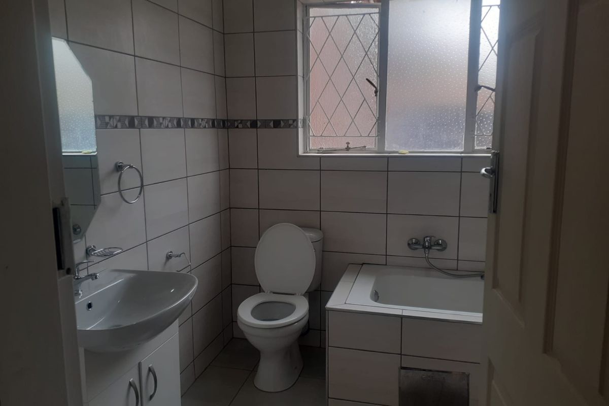 A functional bathroom featuring a vanity cabinet, built-in bathtub, and tiled finishes throughout, providing a practical space for daily use.