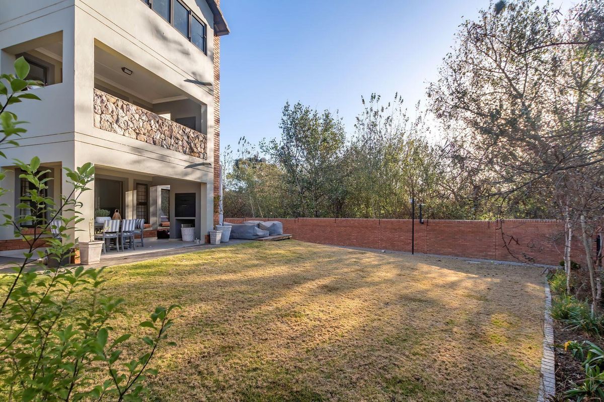 Rear view of the apartment featuring a covered patio with a built-in braai, stone cladding accents, and a private garden with a brick boundary wall.