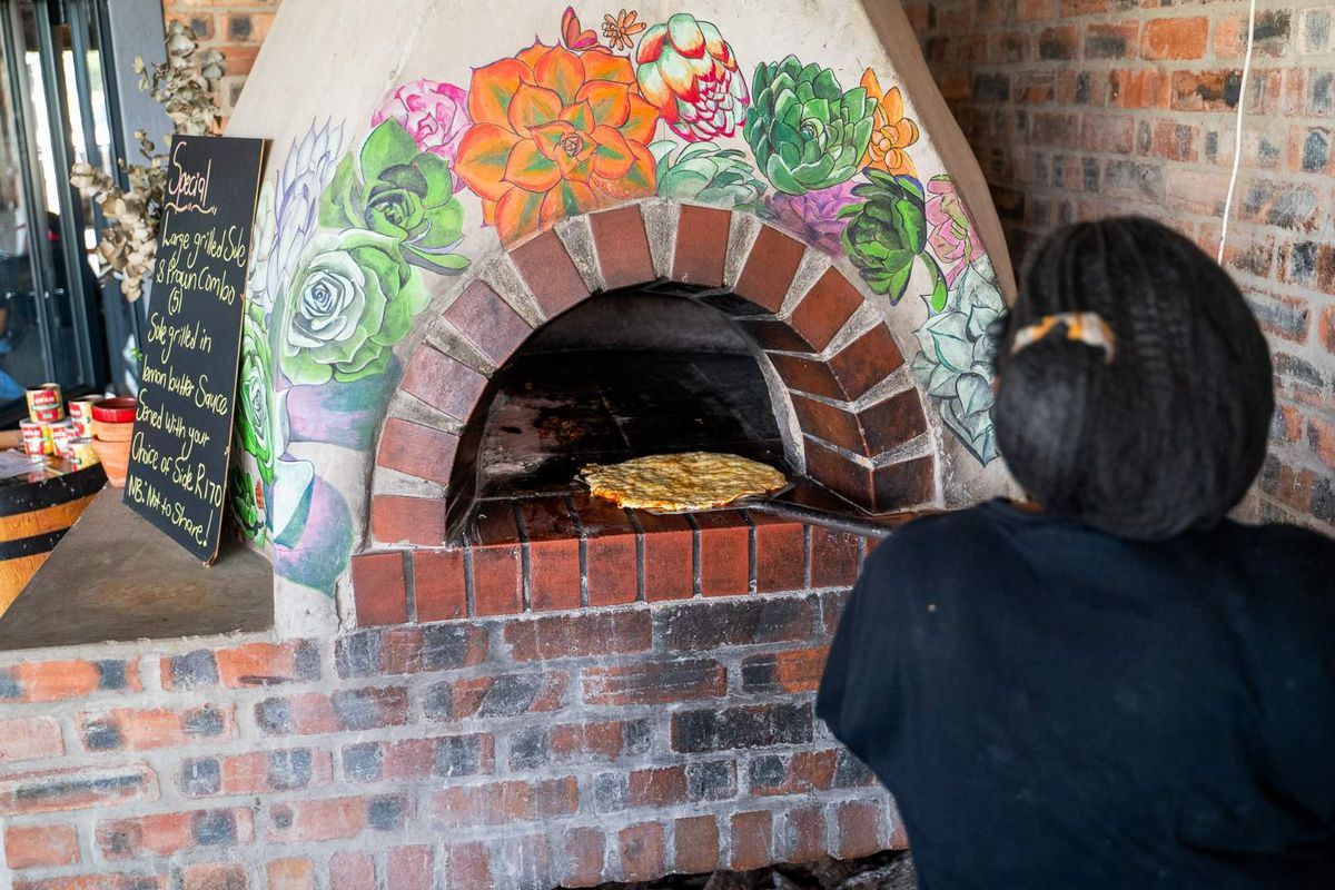 A rustic kitchen area featuring a custom-built brick pizza oven with decorative floral mural painting.