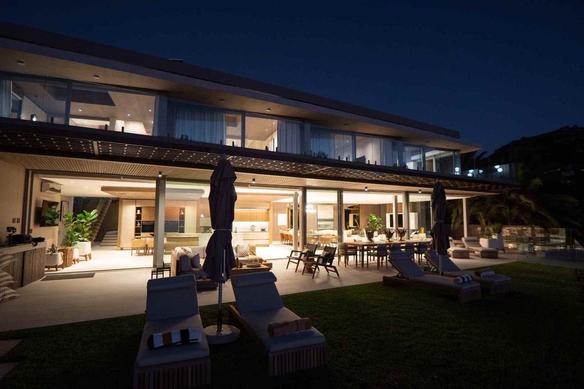 A stunning modern residence at night, featuring expansive glass sliding doors, a covered patio, and seamless indoor-outdoor flow to the garden.