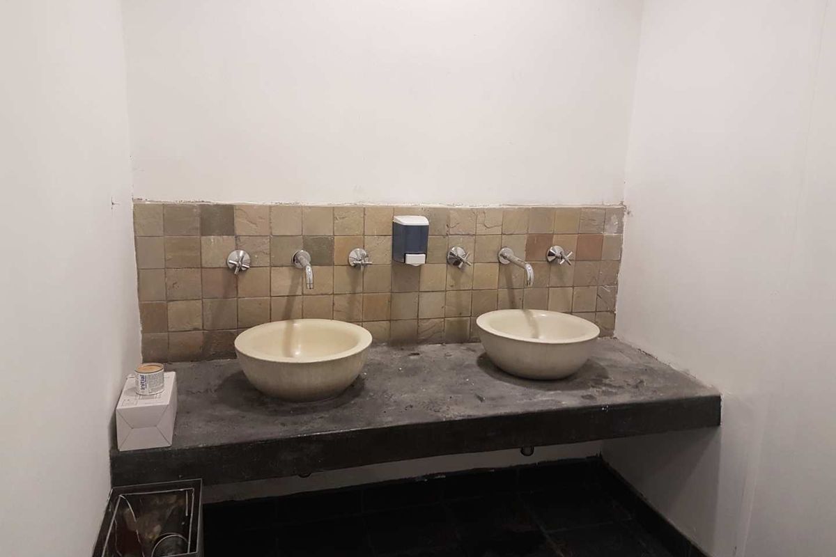 A functional office bathroom featuring a concrete vanity with double vessel sinks and a stone tile backsplash.