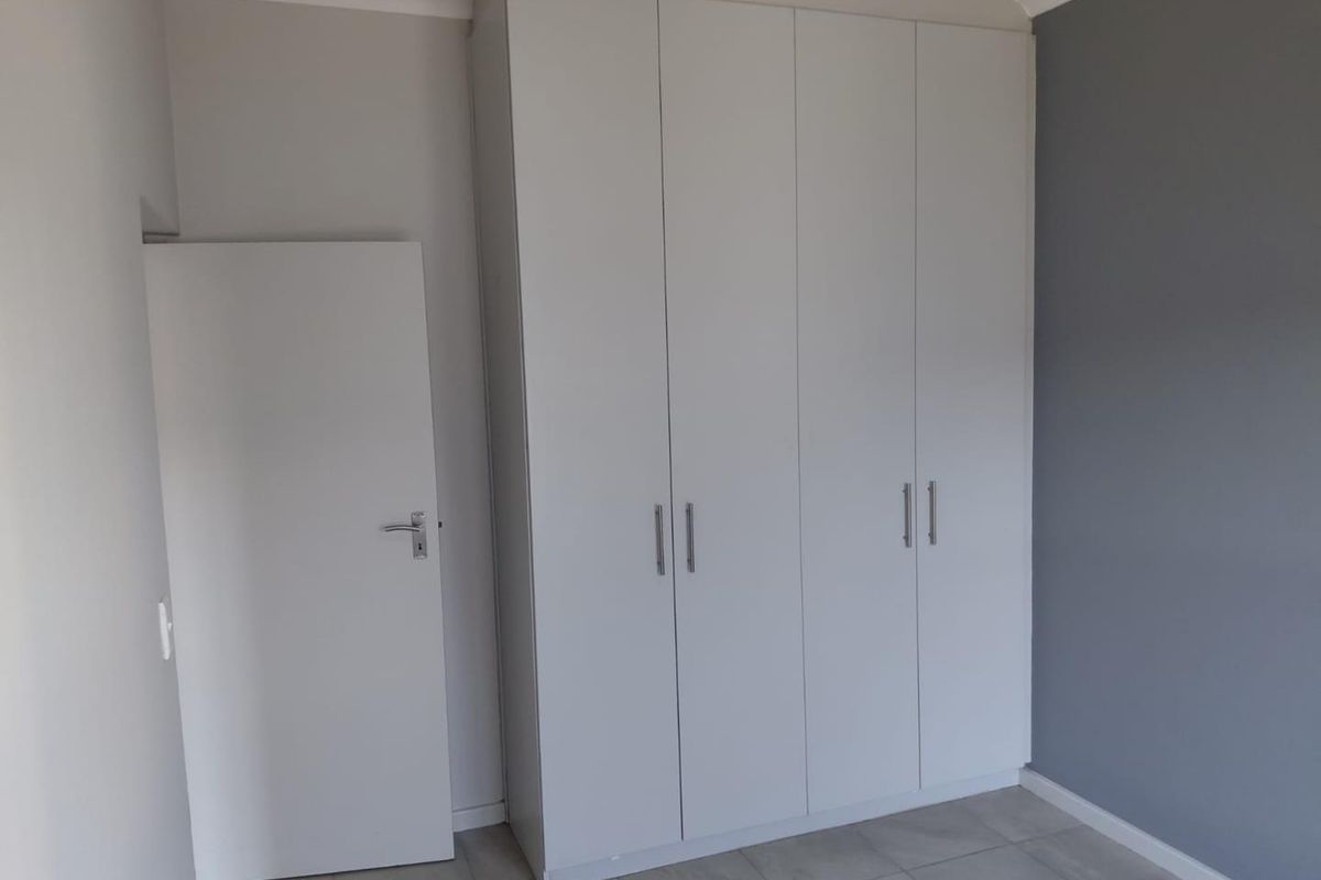 A clean, empty bedroom featuring neutral wall tones, tiled flooring, and modern white built-in cupboards providing ample storage space.