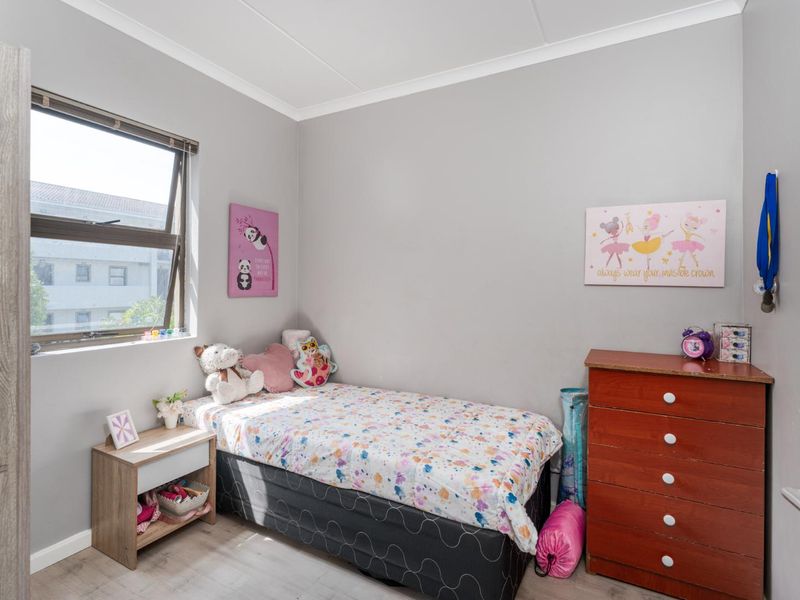 A well-maintained bedroom featuring neutral grey walls, laminate flooring, and a large aluminium-framed window providing natural light.