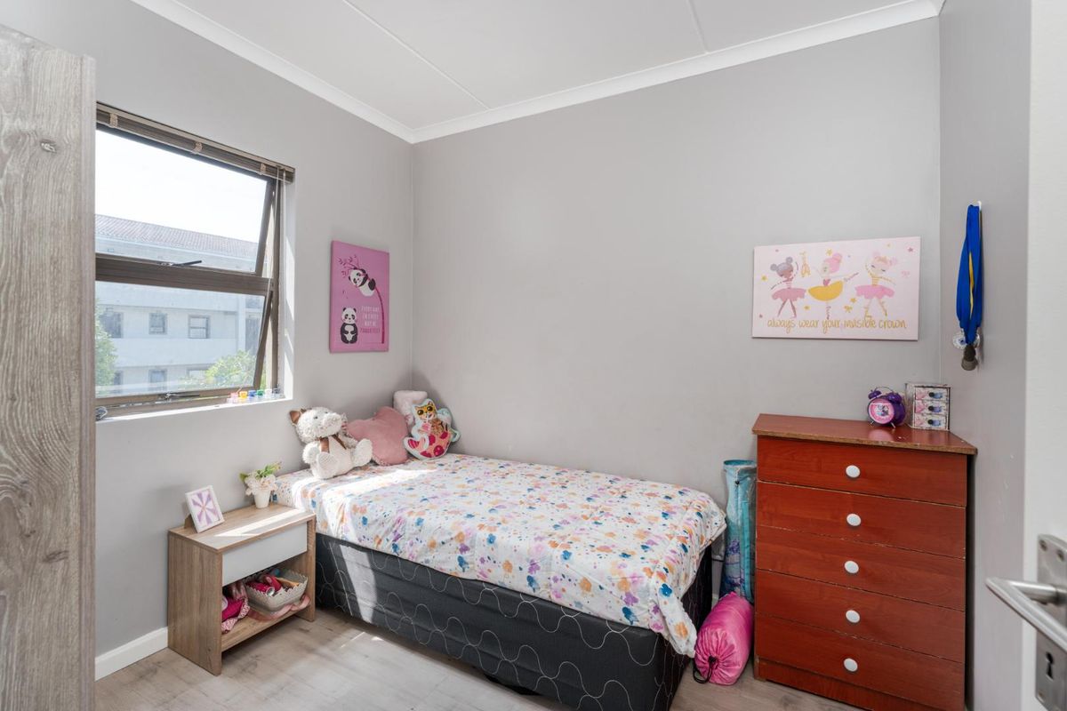 A well-maintained bedroom featuring neutral grey walls, laminate flooring, and a large aluminium-framed window providing natural light.