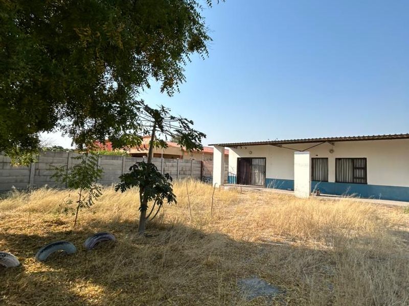 Rear view of the property featuring a covered patio, security bars on windows, and a large backyard area with dry vegetation.