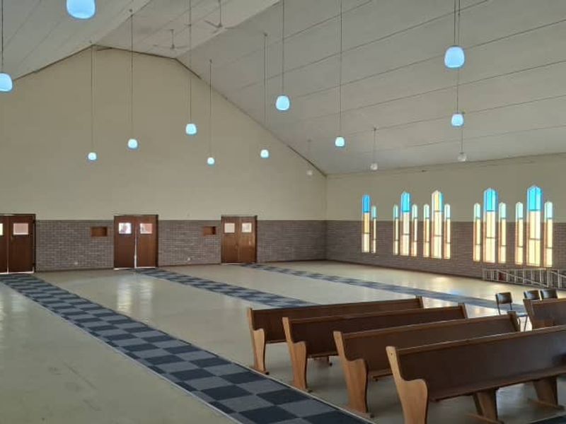 Spacious hall featuring a high vaulted ceiling, numerous pendant lights, and large arched windows, suitable for events or community gatherings.