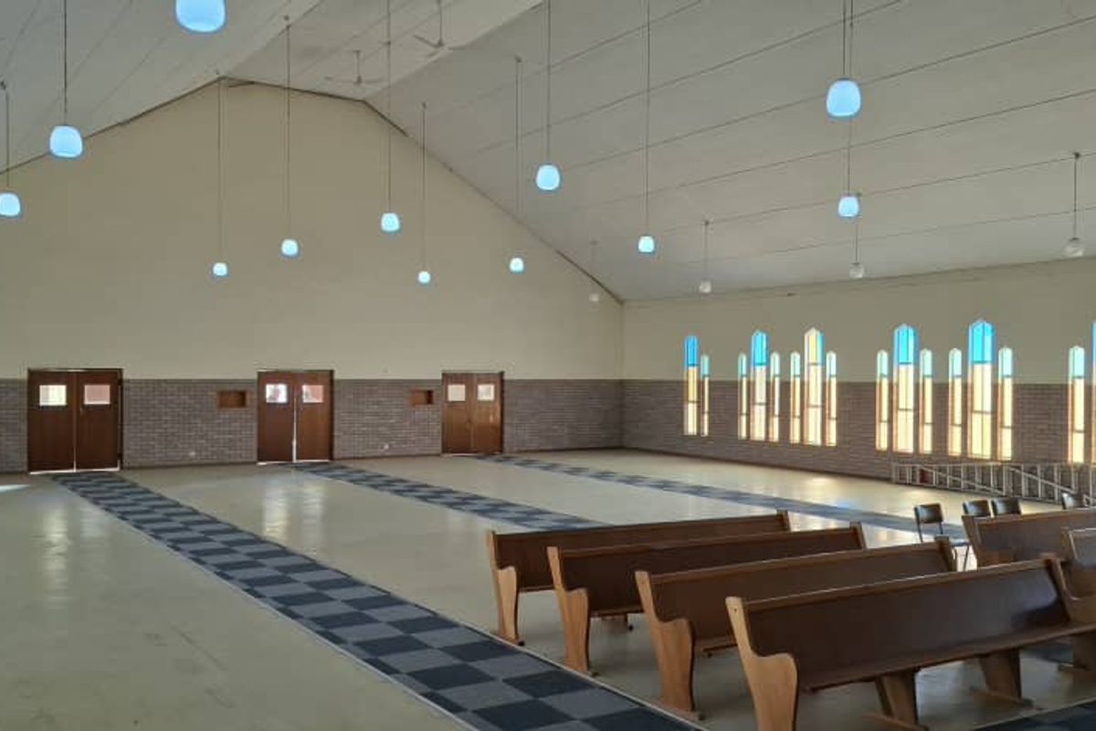 Spacious hall featuring a high vaulted ceiling, numerous pendant lights, and large arched windows, suitable for events or community gatherings.