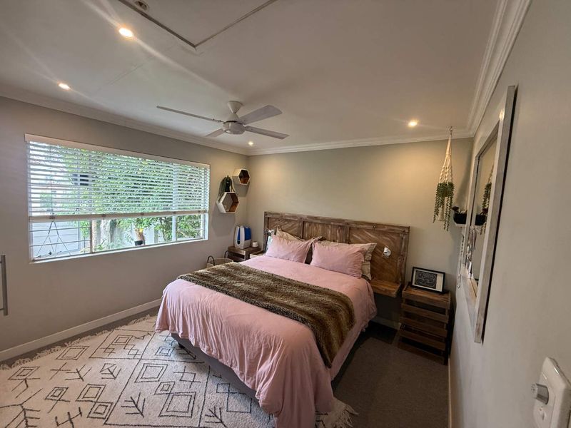 A well-maintained bedroom featuring recessed downlights, a ceiling fan, and crown molding, with large windows fitted with venetian blinds.