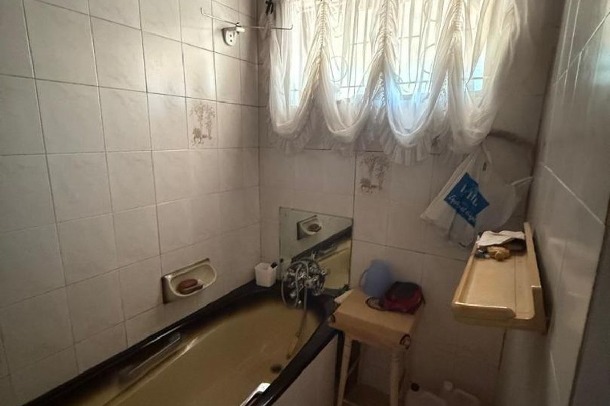 A dated bathroom featuring a built-in bathtub, ceramic wall and floor tiling, and a ventilation grille. The space would benefit from modern updates.