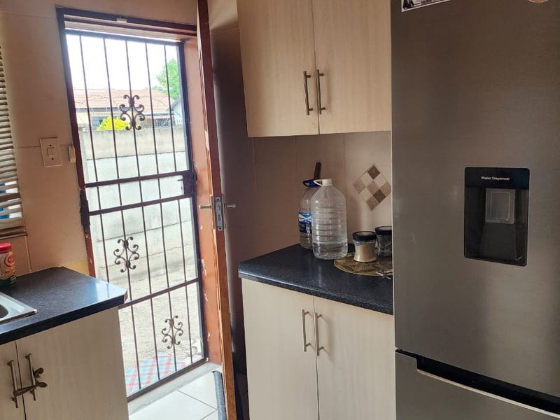Compact kitchen area featuring laminate cabinetry, dark countertops, a stainless steel sink, and direct access to the exterior via a security gate.