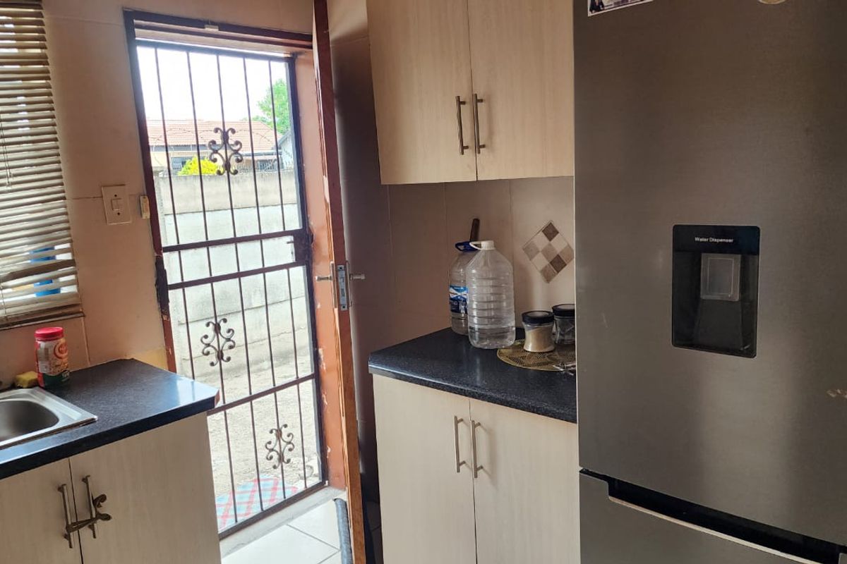Compact kitchen area featuring laminate cabinetry, dark countertops, a stainless steel sink, and direct access to the exterior via a security gate.