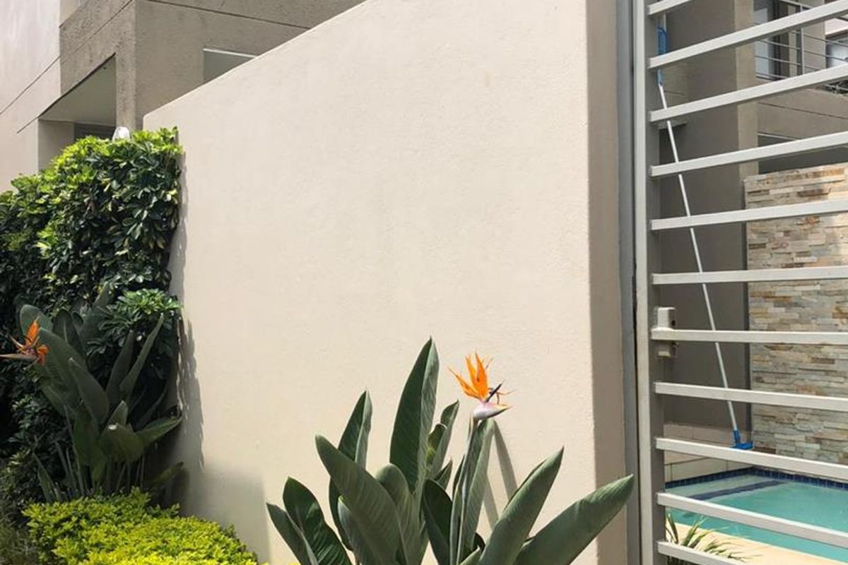 A well-maintained rear exterior area featuring a private swimming pool, stone-clad feature wall, metal security gate, and a balcony above.