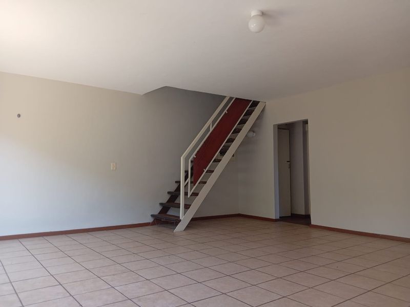 An empty, open-plan living area featuring tiled flooring and a central staircase leading to the upper level.