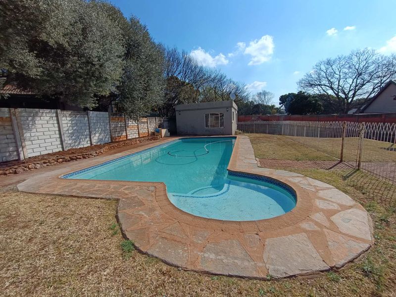 A backyard swimming pool area featuring stone paving, a boundary wall, and a small outbuilding set within a garden space.