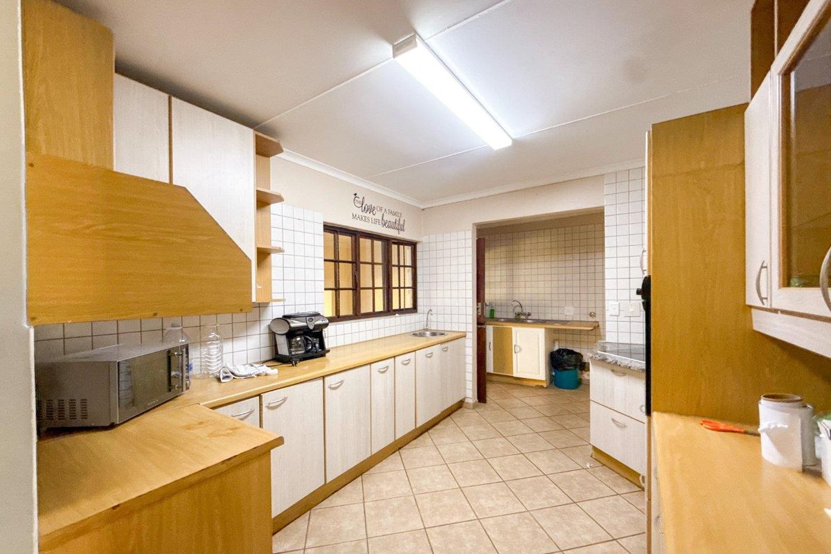 A functional kitchen featuring laminate cabinetry, tiled backsplash, and ceramic flooring, with an adjoining scullery area providing additional prep and wash-up space.